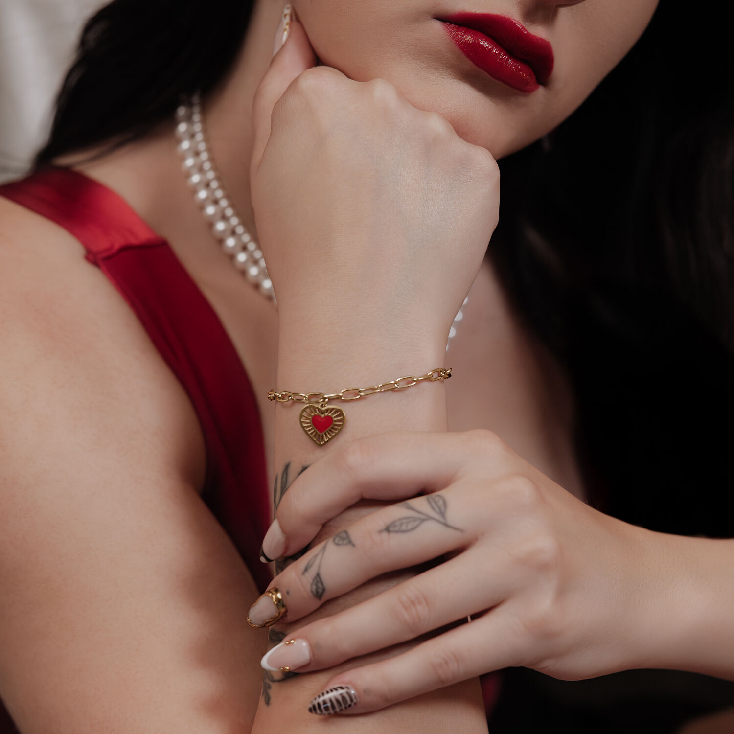 Donna indossa braccialetto Golden Sacred Heart, abito rosso, collana di perle