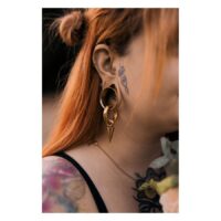 Donna con capelli rossi indossa Labret Push-Fit Monstera dorato nell'orecchio, tatuaggi visibili