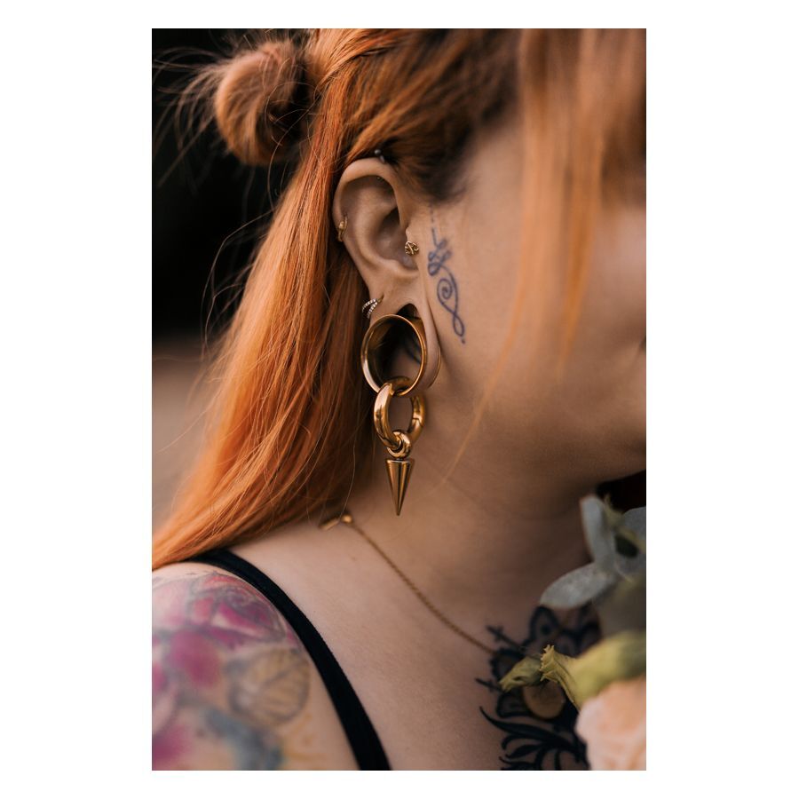 Donna con capelli rossi indossa Labret Push-Fit Monstera dorato nell'orecchio, tatuaggi visibili