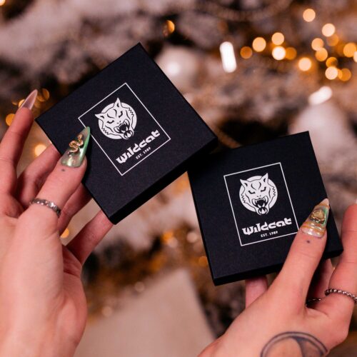 Due scatole regalo nere con logo Wildcat, tenute da mani con unghie dorate