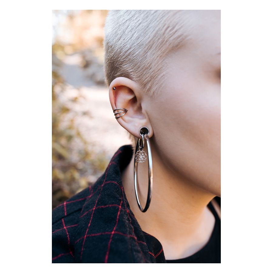 Persona con 3 Clicker Ring in Nero e Argento nell'orecchio, sfondo naturale