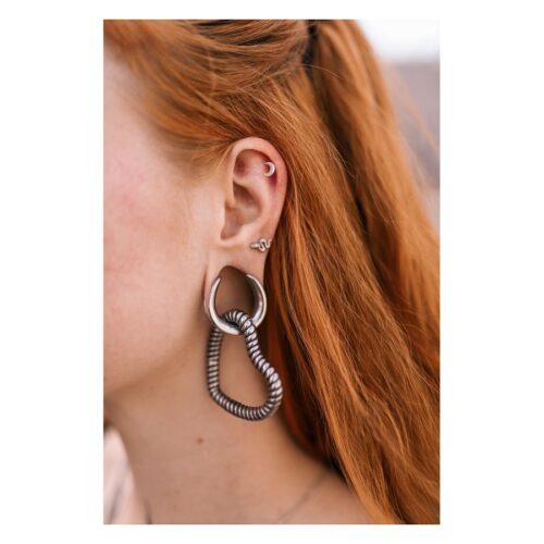 Barbell a forma di serpente in argento nell'orecchio di una persona con capelli rossi, primo piano