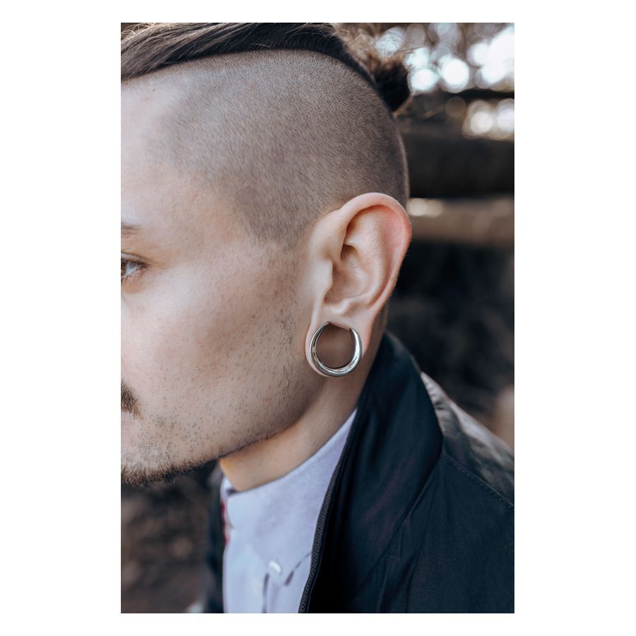 Uomo con Ear Saddles argentati nell'orecchio davanti a uno sfondo sfocato