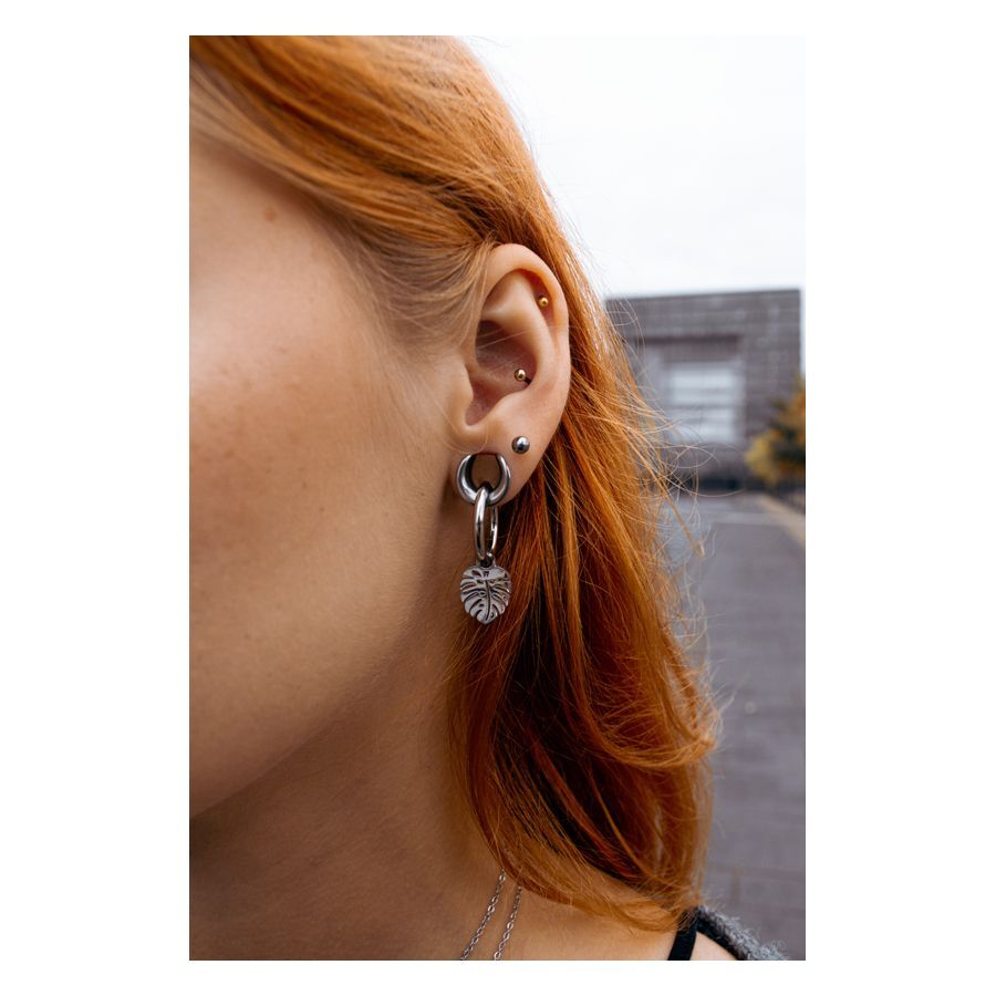 Selle auricolari nere in acciaio chirurgico con ciondolo a foglia indossate su un orecchio