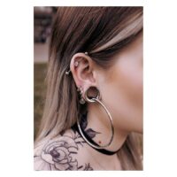 Ear Saddles in argento e nero su un orecchio con piercing, tatuaggio sullo sfondo