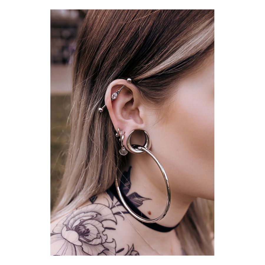 Ear Saddles in argento e nero su un orecchio con piercing, tatuaggio sullo sfondo