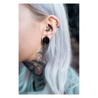 Primo piano di un orecchio con neri Monstera Ear Saddles e altri piercing, sfondo sfocato