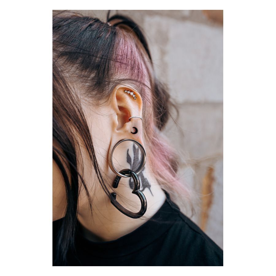 Orecchio con più piercing, incluso un Luna Earbarbell nero e un grande tunnel, ciocca di capelli rosa
