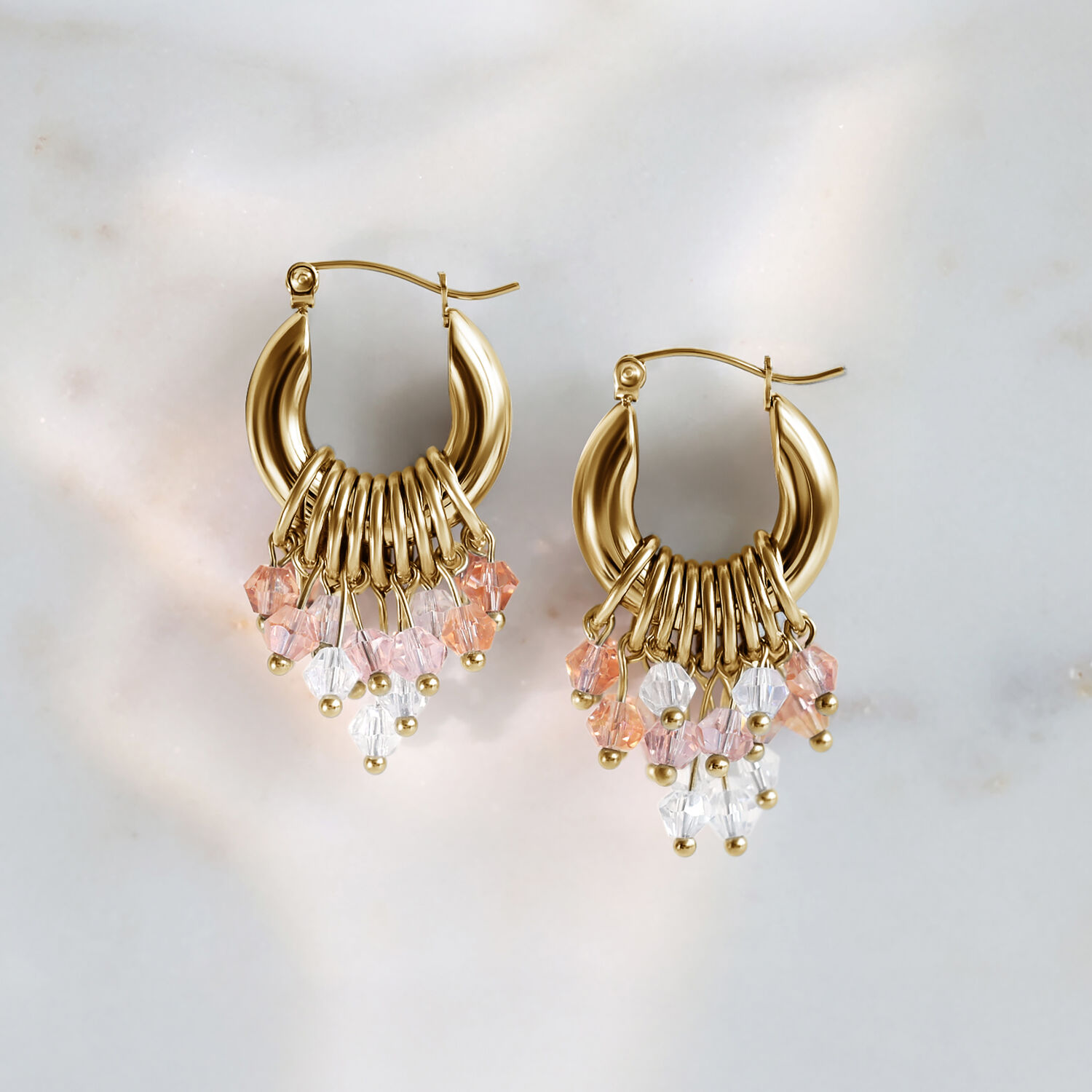 Orecchini Glamour Hoops dorati con cristalli rosa e chiari su sfondo di marmo