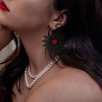 Donna indossa orecchini Sacred Heart Hoops neri con dettaglio a cuore rosso, primo piano