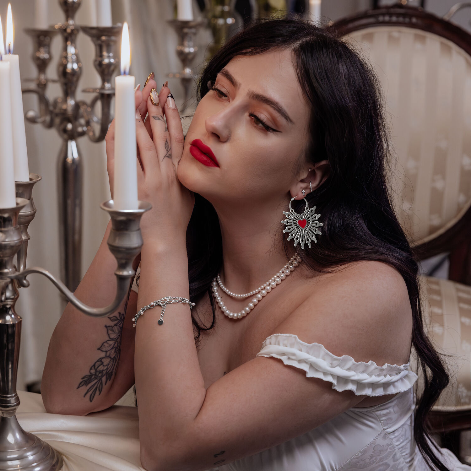 Donna con lunghi capelli scuri indossa gli orecchini a cerchio Sacred Heart in nero e argento, seduta a un tavolo con candelabro.