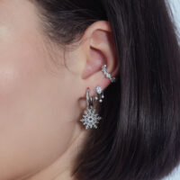 Pendente in cristallo d'argento all'orecchio con altri piercing su sfondo bianco