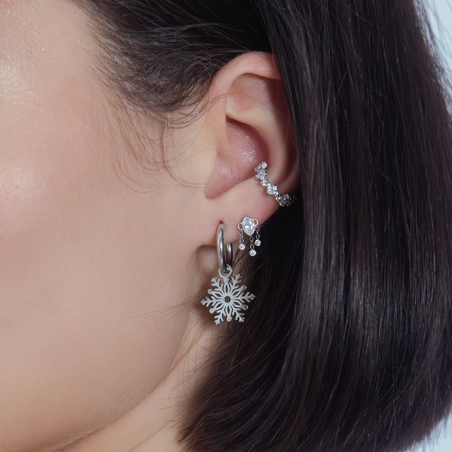 Pendente in cristallo d'argento all'orecchio con altri piercing su sfondo bianco