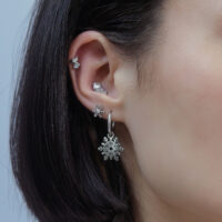 Orecchio con diversi piercing in argento, design a fiocco di neve, su sfondo neutro