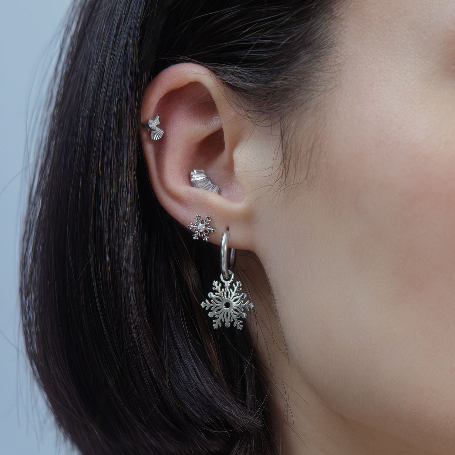 Orecchio con diversi piercing in argento, design a fiocco di neve, su sfondo neutro