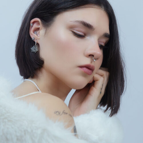 Donna con piercing a fiocco di neve in argento nell'orecchio su sfondo chiaro
