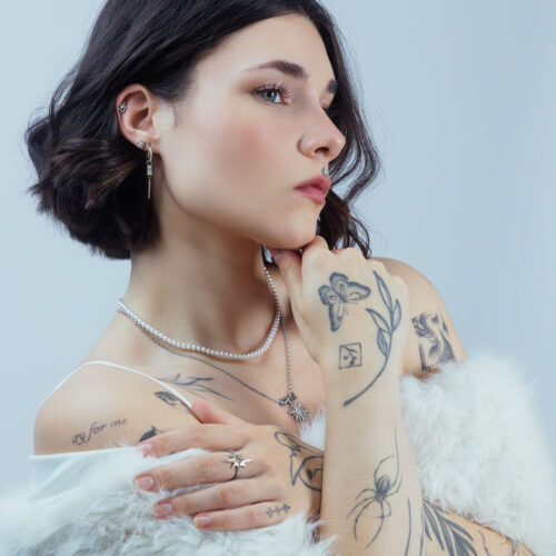 Donna con diversi piercing, incluso un attacco Sunburst argento nell'orecchio, su sfondo neutro