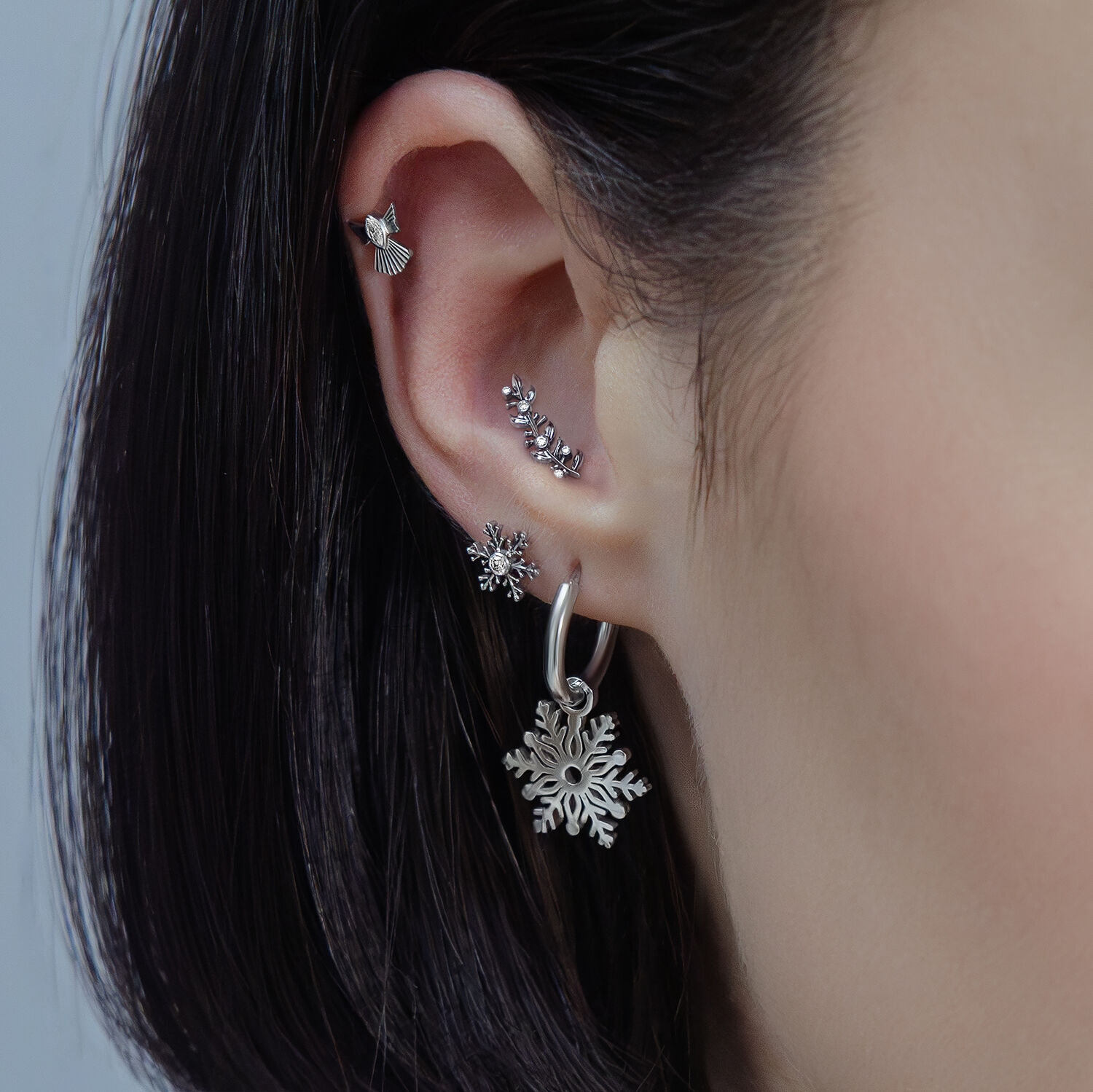 Primo piano di un orecchio con diversi piercing in argento di vari design e cristalli