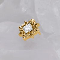 Accessorio in metallo dorato con cristallo chiaro su sfondo grigio