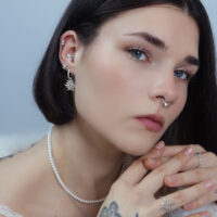 Donna con diversi piercing, incluso un attacco Snow Angel in argento nell'orecchio, su sfondo neutro.