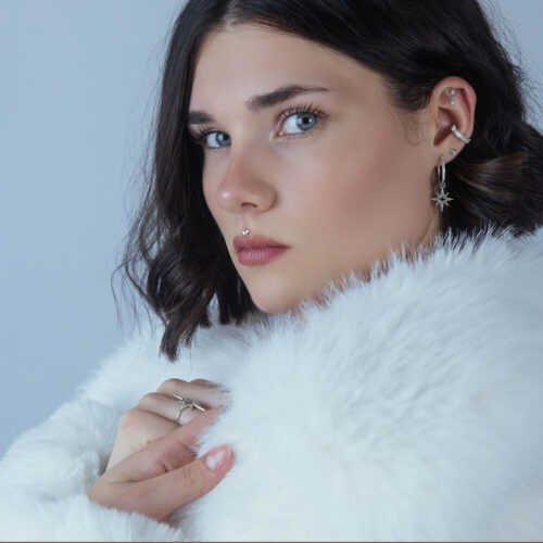 Donna con piercing all'elica e doppio accessorio in argento su sfondo chiaro