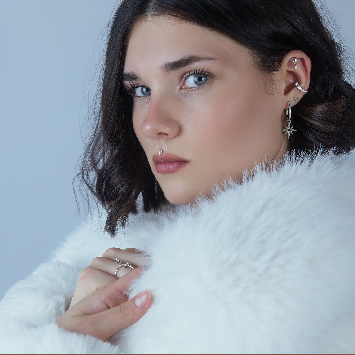 Donna con piercing all'elica e doppio accessorio in argento su sfondo chiaro