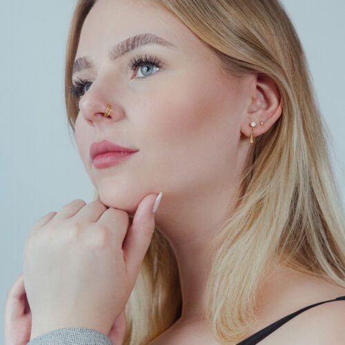 Donna con piercing clicker dorato all'orecchio, profilo laterale su sfondo chiaro