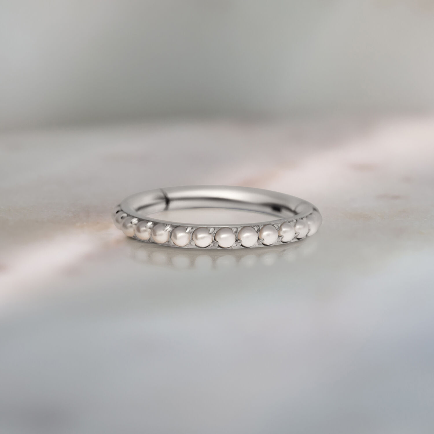 Anello piercing in argento con decorazione di perle su sfondo grigio