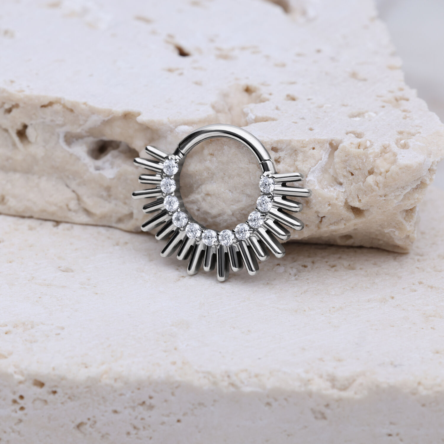 Clicker per setto in argento con design a raggi su sfondo di pietra chiara