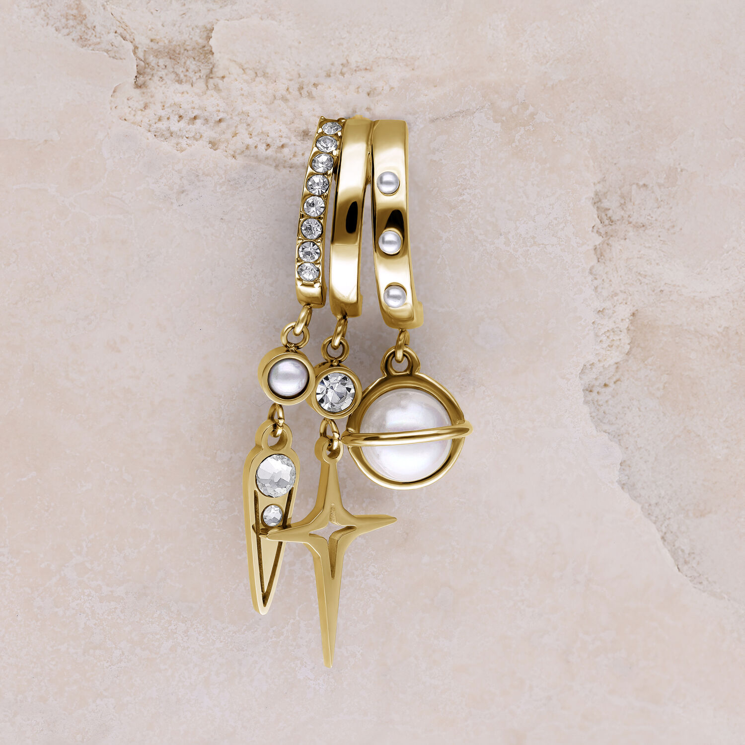 Orecchini dorati con perle e pietre scintillanti Tre orecchini dorati con perle, pietre scintillanti e ciondolo a stella su sfondo beige