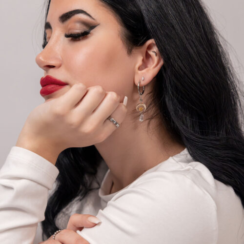 Donna con lunghi capelli neri indossa orecchini pendenti in acciaio inossidabile argento su sfondo neutro