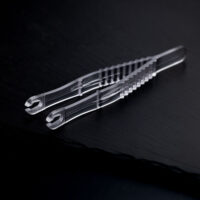Due pinze da piercing rotonde e sterili trasparenti incrociate su uno sfondo scuro.