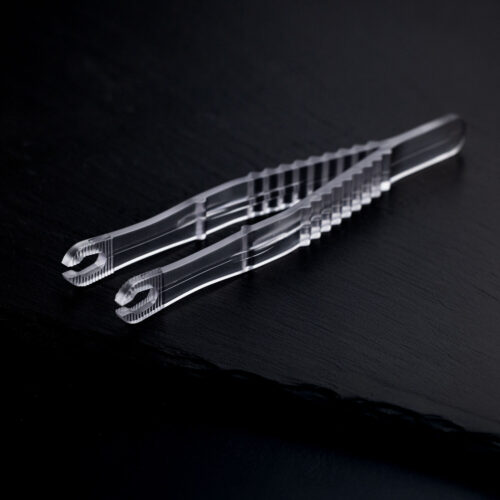 Due pinze da piercing rotonde e sterili trasparenti incrociate su uno sfondo scuro.
