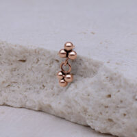Piercing in rosé gold con tre sfere su sfondo chiaro
