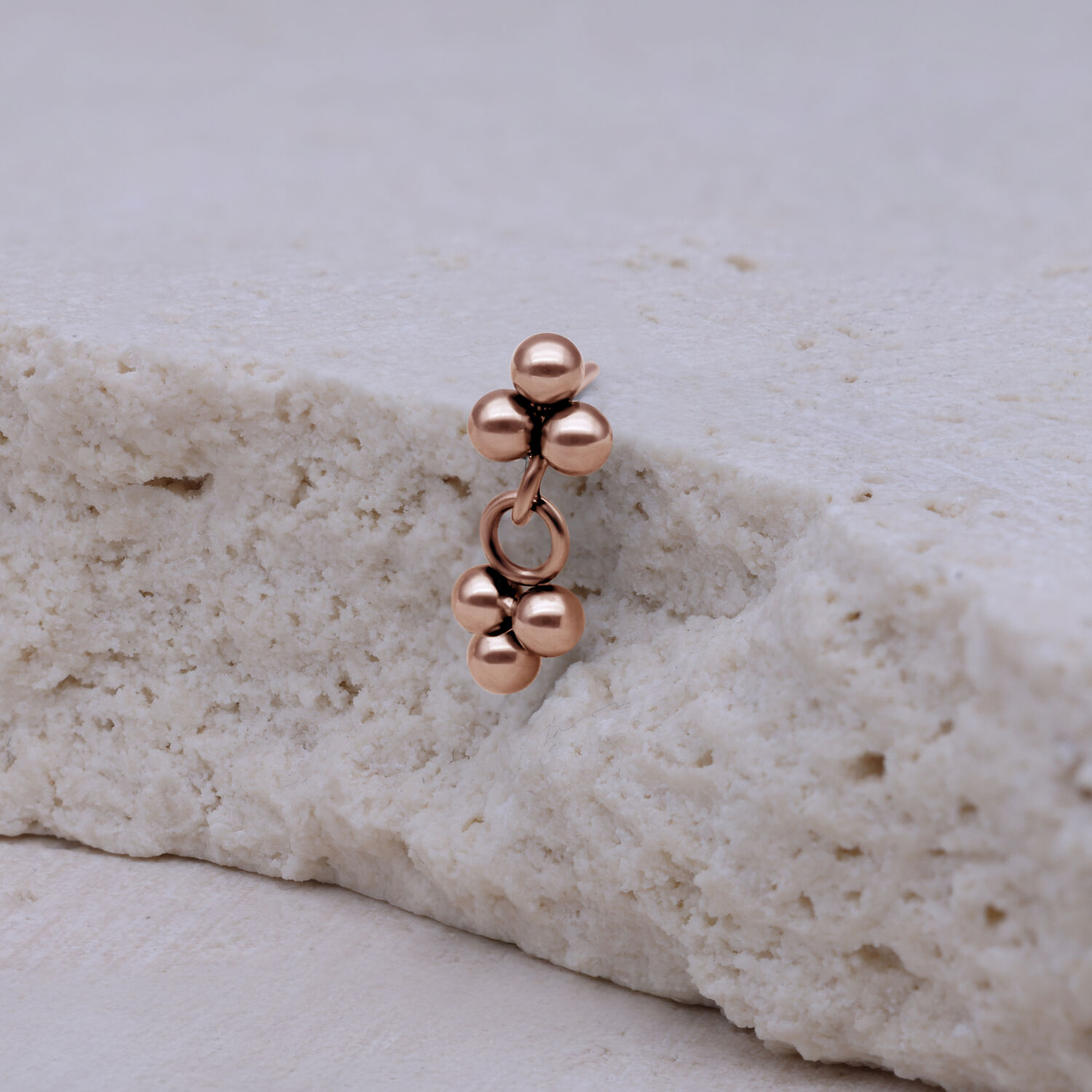 Piercing in rosé gold con tre sfere su sfondo chiaro
