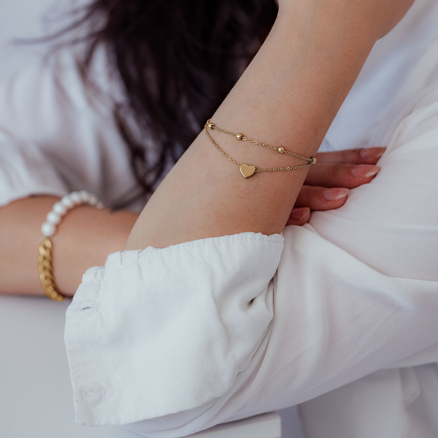 Bracciale a cuore a doppio filo in oro al polso di una persona con camicia bianca