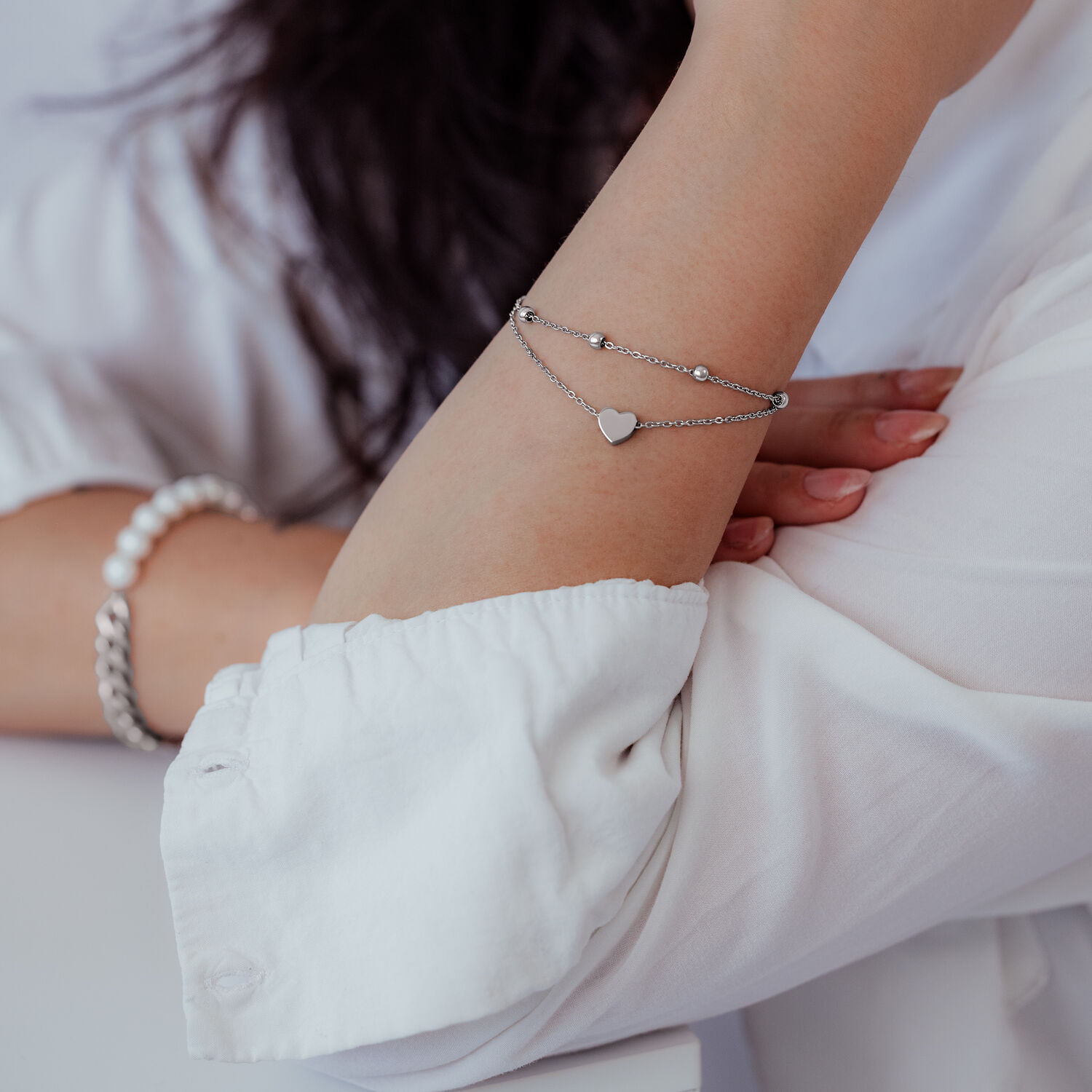 Bracciale a doppio filo in argento con ciondolo a cuore sul braccio di una persona con abbigliamento bianco