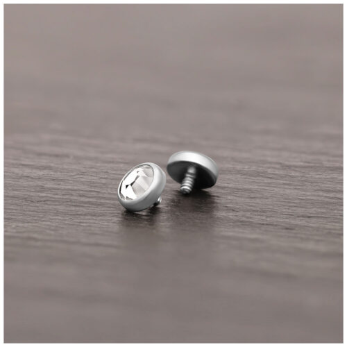 Punta piercing in titanio argento con cristallo chiaro su superficie di legno