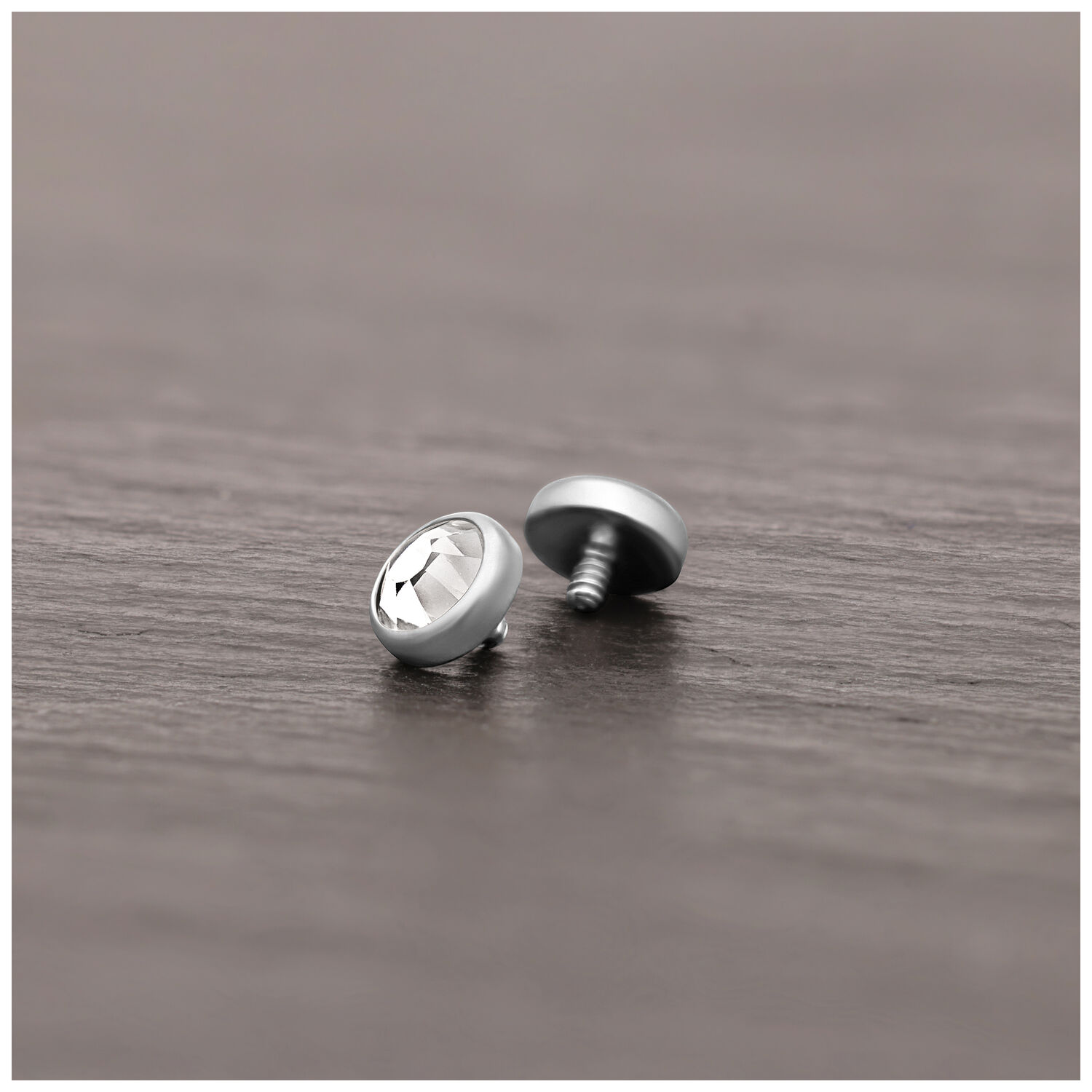 Punta piercing in titanio argento con cristallo chiaro su superficie di legno