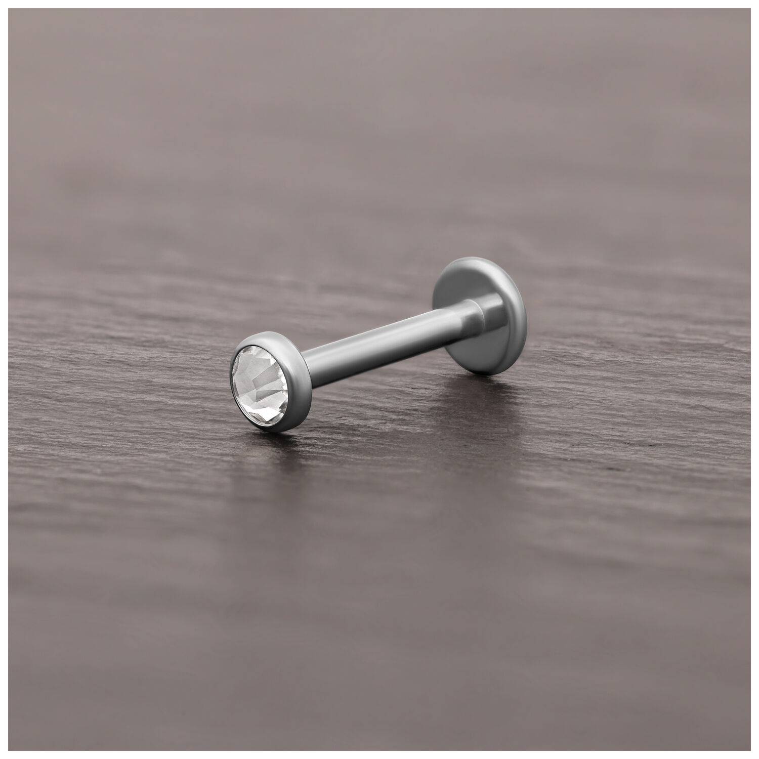 Punta per piercing in titanio argento con cristallo chiaro su superficie di legno scuro