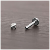 Attacco per piercing in titanio argento con cristallo chiaro su legno scuro.