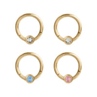Quattro anelli piercing dorati con cristalli chiari, blu, rosa e scintillanti su sfondo bianco
