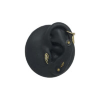 Modello di orecchio in silicone nero con attacchi dorati per piercing su sfondo bianco