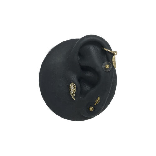 Modello di orecchio in silicone nero con attacchi dorati per piercing su sfondo bianco