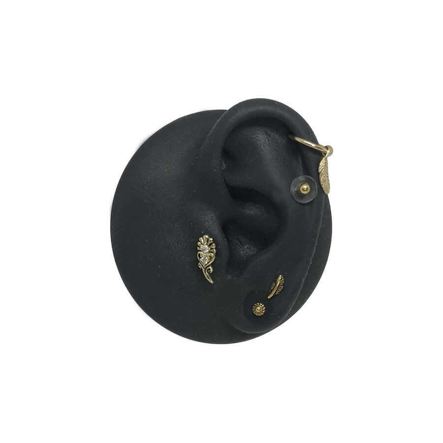 Modello di orecchio in silicone nero con attacchi dorati per piercing su sfondo bianco