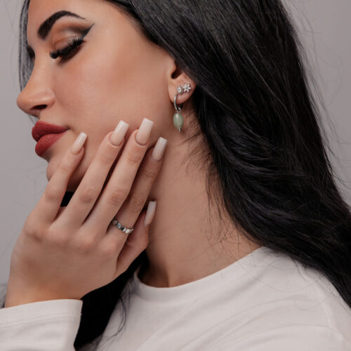 Donna con lunghi capelli neri indossa orecchini in avventurina verde e maglione bianco