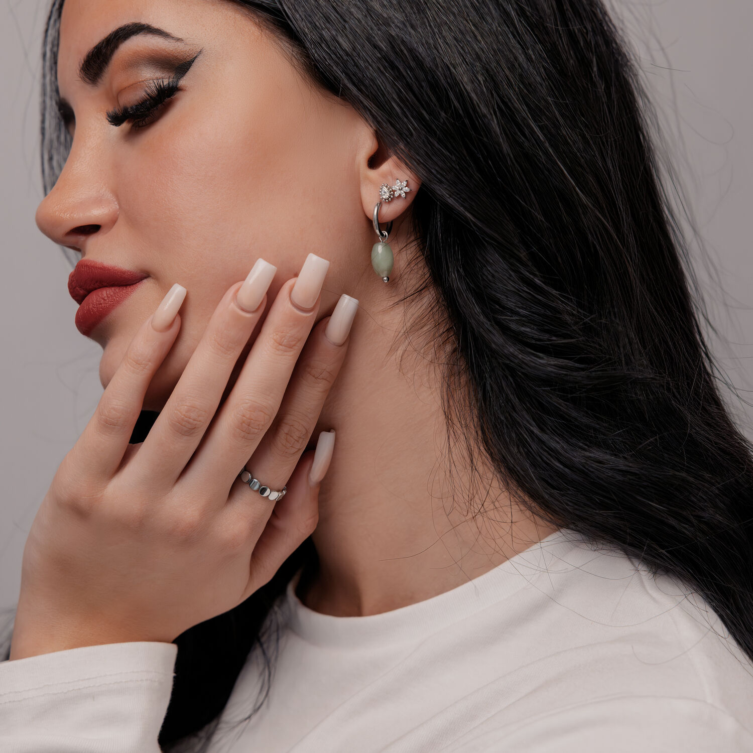 Donna con lunghi capelli neri indossa orecchini in avventurina verde e maglione bianco
