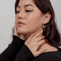 Donna con orecchini libellula dorati, top nero, parete bianca
