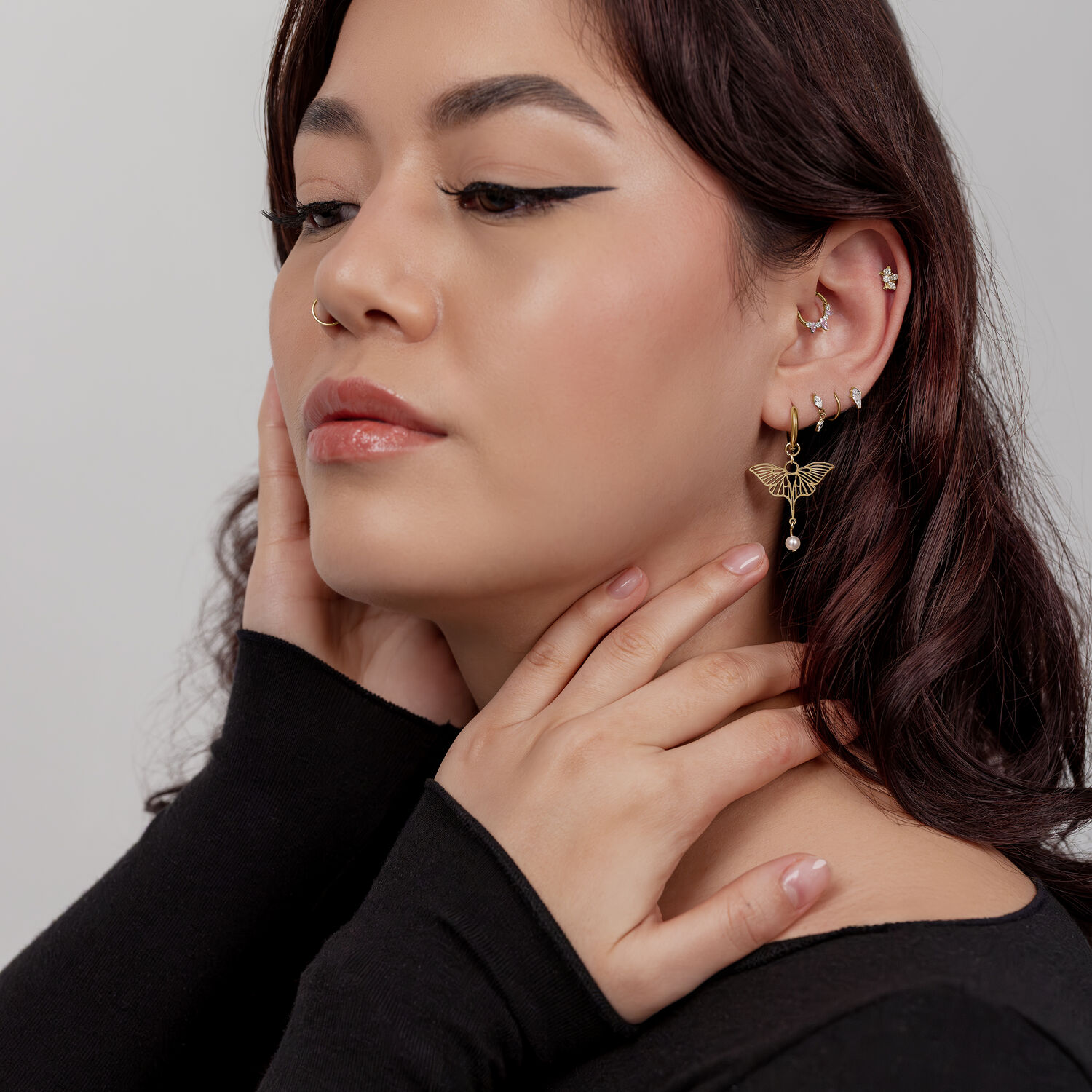 Donna con orecchini libellula dorati, top nero, parete bianca