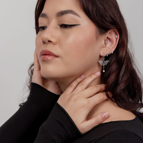 Donna con diversi orecchini, tra cui un orecchino a libellula con perla, su sfondo chiaro